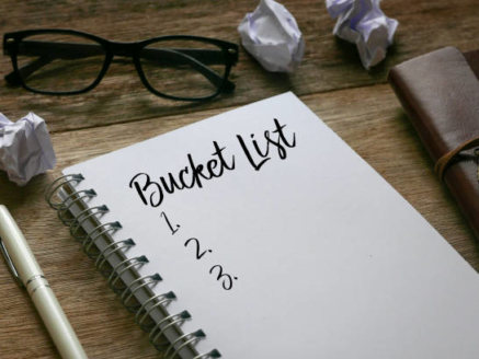 Pen,trash paper,sunglasses, and notebook written with Bucket List on wooden background.